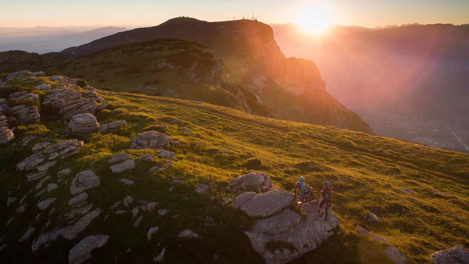 Due ciclisti si godono il tramonto su Andalo da una delle montagne circostanti